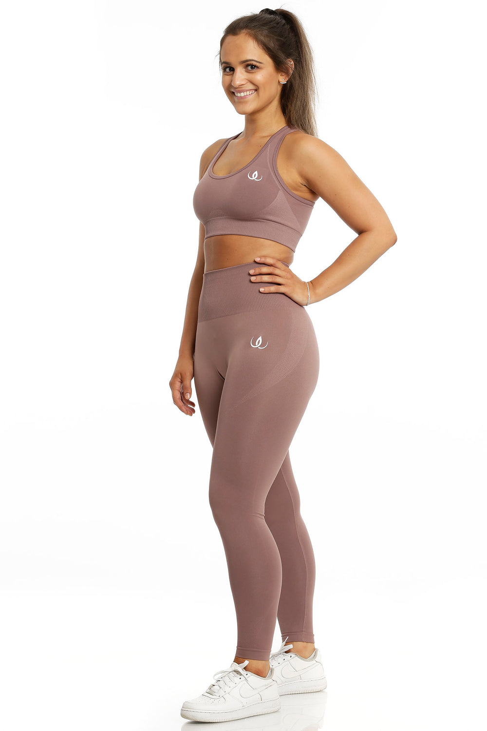 Sport-BH und Leggings im gleichen rosébraunen Ton. Das Model steht mit der Hand an der Hüfte, in weißen Schuhen.