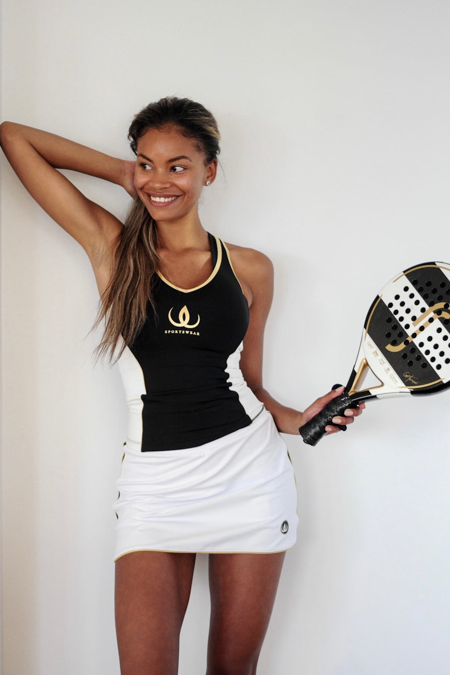 Das Model steht an der Wand im weißen Rock und einem schwarzen Top mit Goldkante.