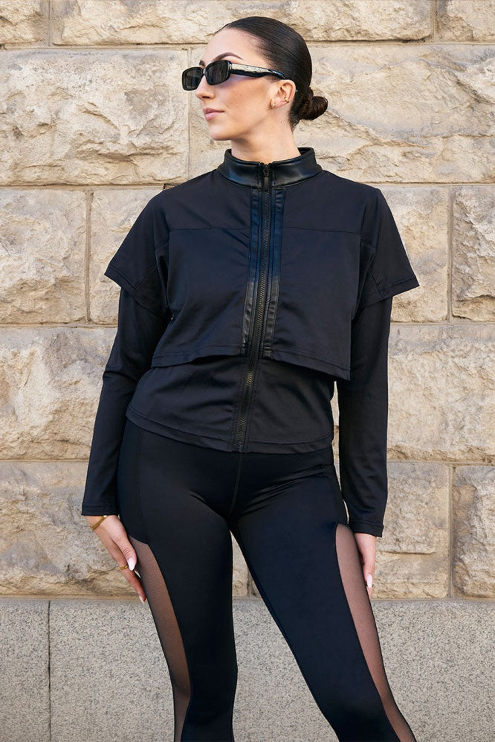 Edge Schwarze Trainingsjacke mit glänzendem Kragen und Lagen über den Schultern, getragen zu schwarzen Leggings mit Mesh.