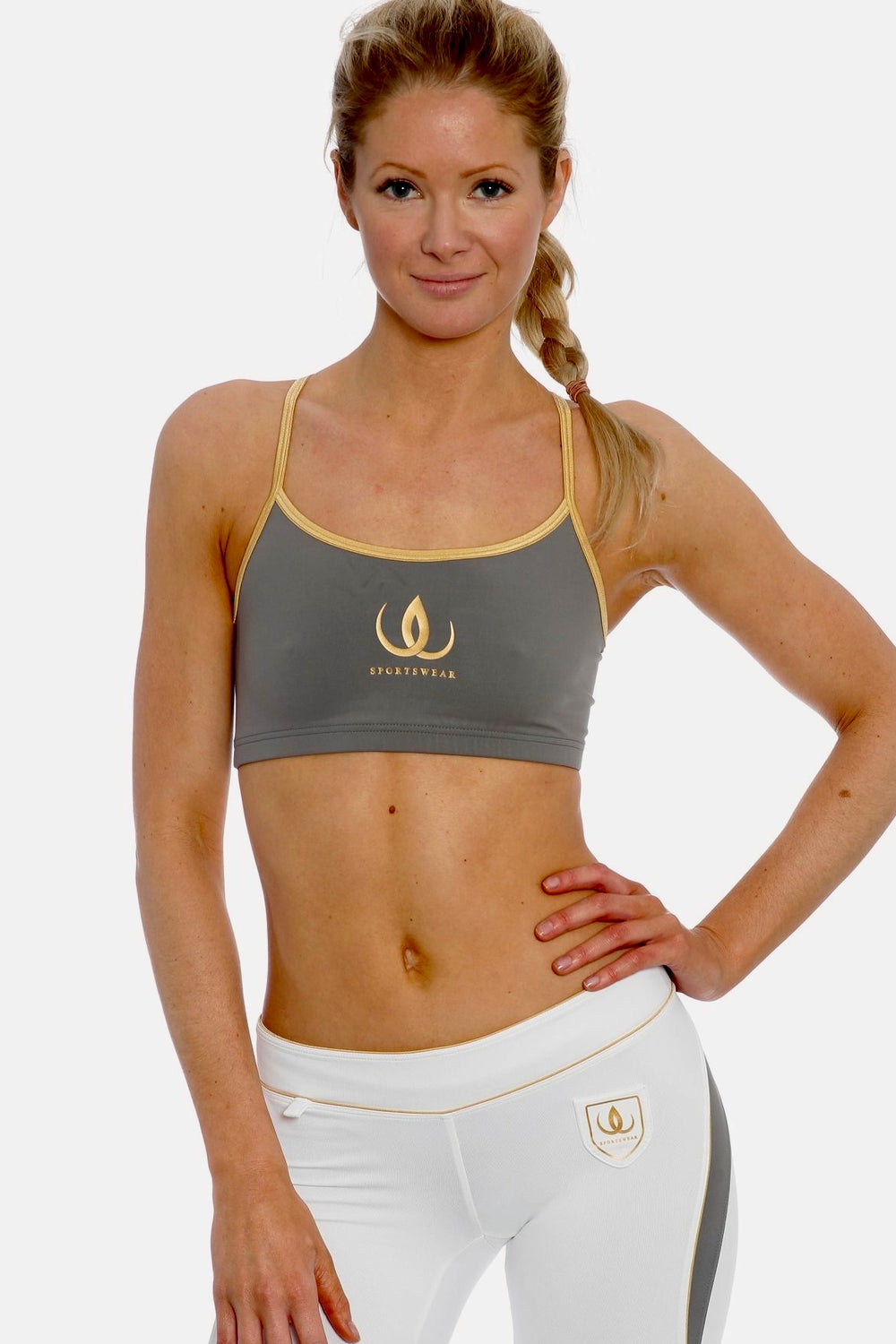 Graues Trainingstop mit goldfarbenen Trägern und Goldlogo, zu weißen Leggings mit grauem Panel.
