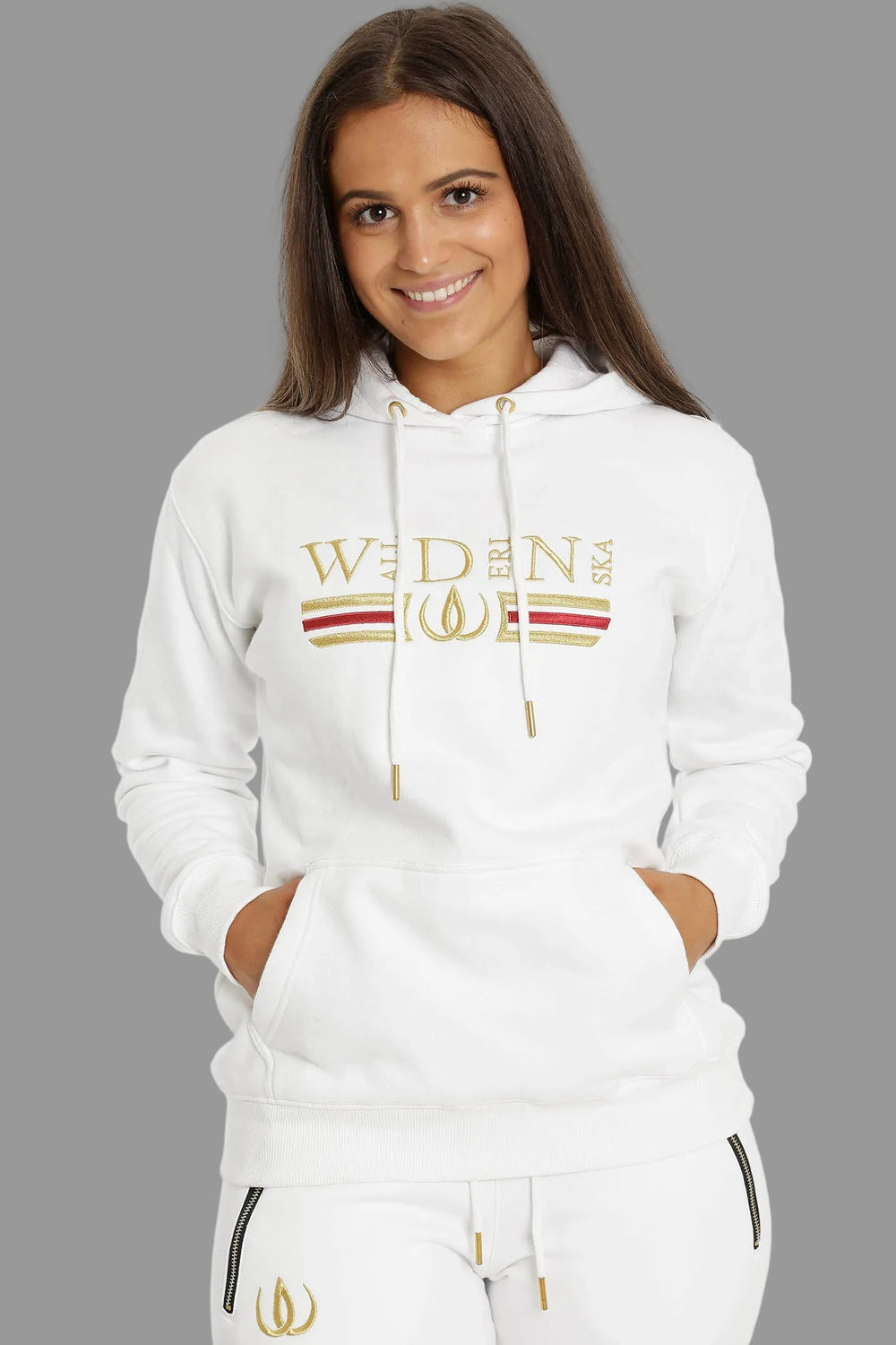 Weißer Hoodie mit Stickerei in Gold und Rot über der Brust, getragen zu weißen Joggers mit Goldlogo.