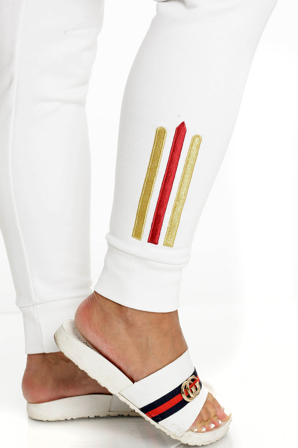 Am Knöchel der weißen Hose sitzen zwei Goldstreifen und ein roter, über einem gerippten Bündchen.