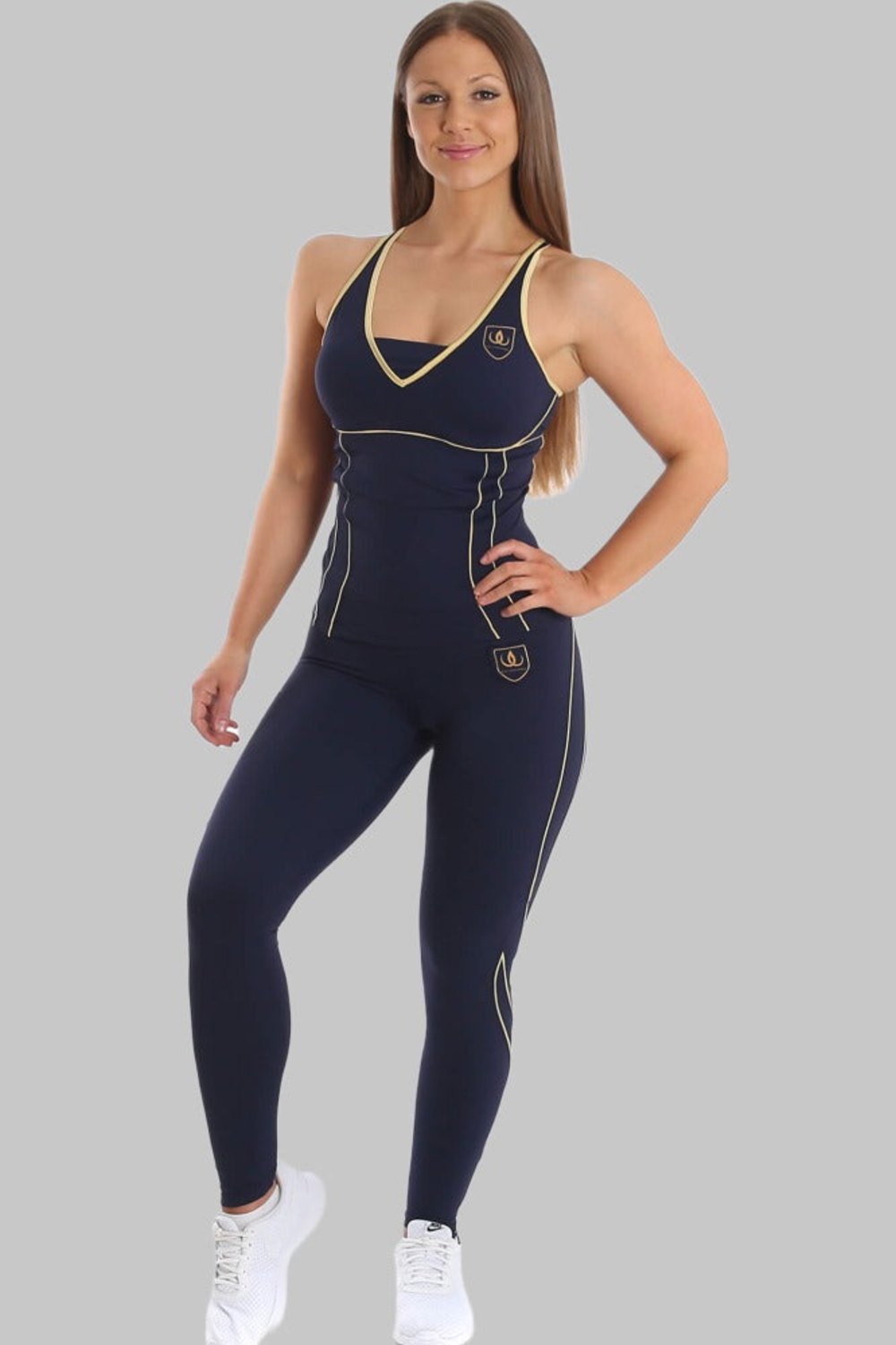 Das Model steht in marineblauem Trainingstop und marineblauen Leggings mit Goldlinien, dazu weiße Sneaker.