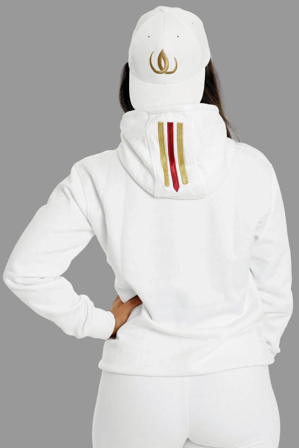 Rückseite des weißen Hoodies mit zwei Goldstreifen und einem roten auf der Kapuze. Das Model trägt eine weiße Cap.
