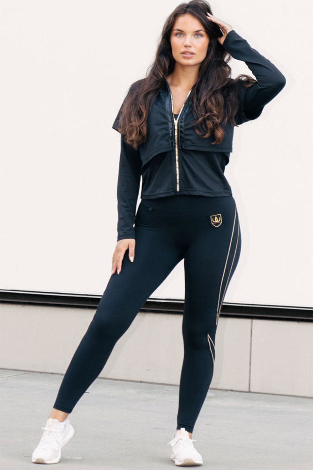 Der goldfarbene Reißverschluss verläuft über die gesamte Jacke, getragen zu schwarzen Leggings mit Goldlinien.