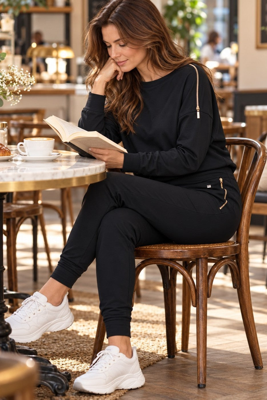 Das Edge Casual Zip Set in Schwarz in einem Café, mit einem Buch und einer Tasse Kaffee.